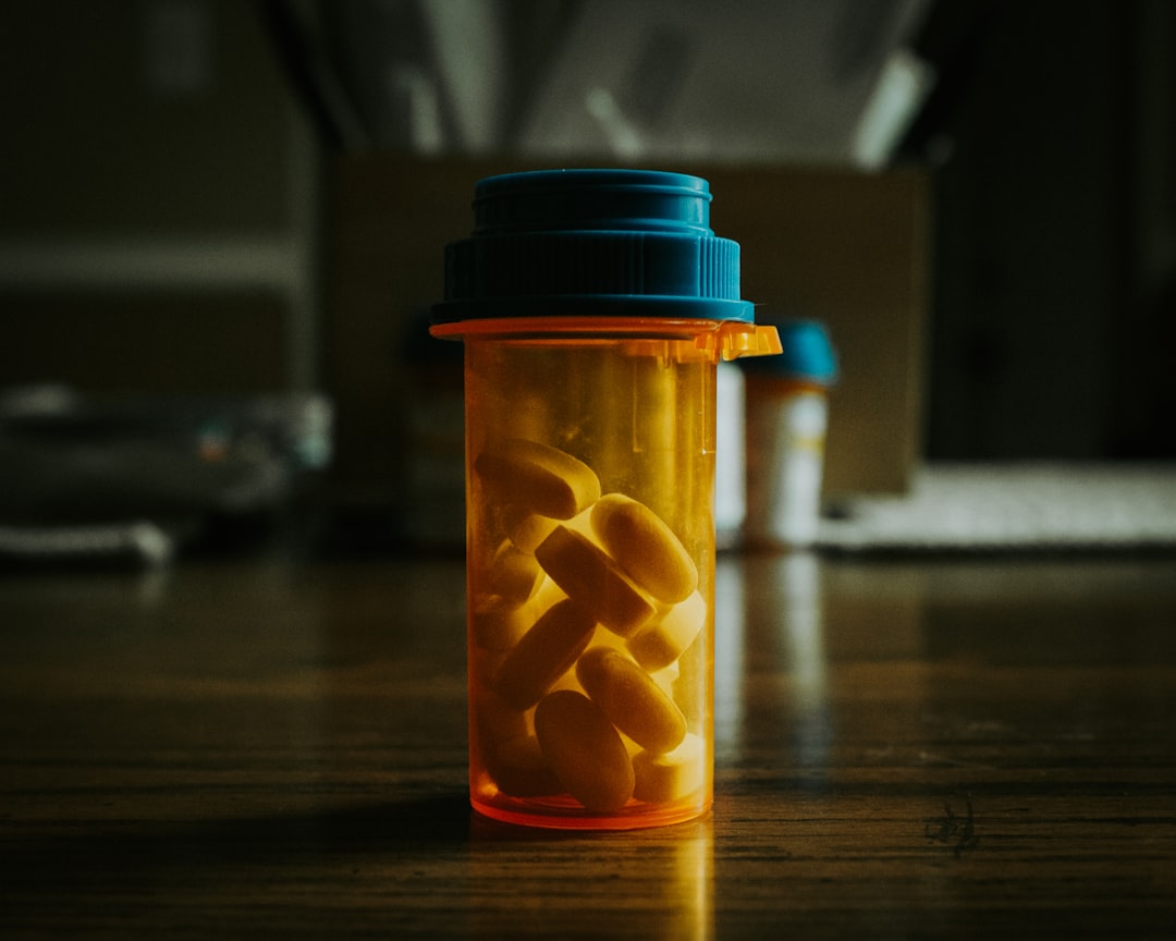 A prescription bottle filled with yellow pills sitting on a wooden table.