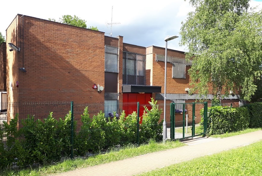 A modern brick building surrounded by greenery and a fence.